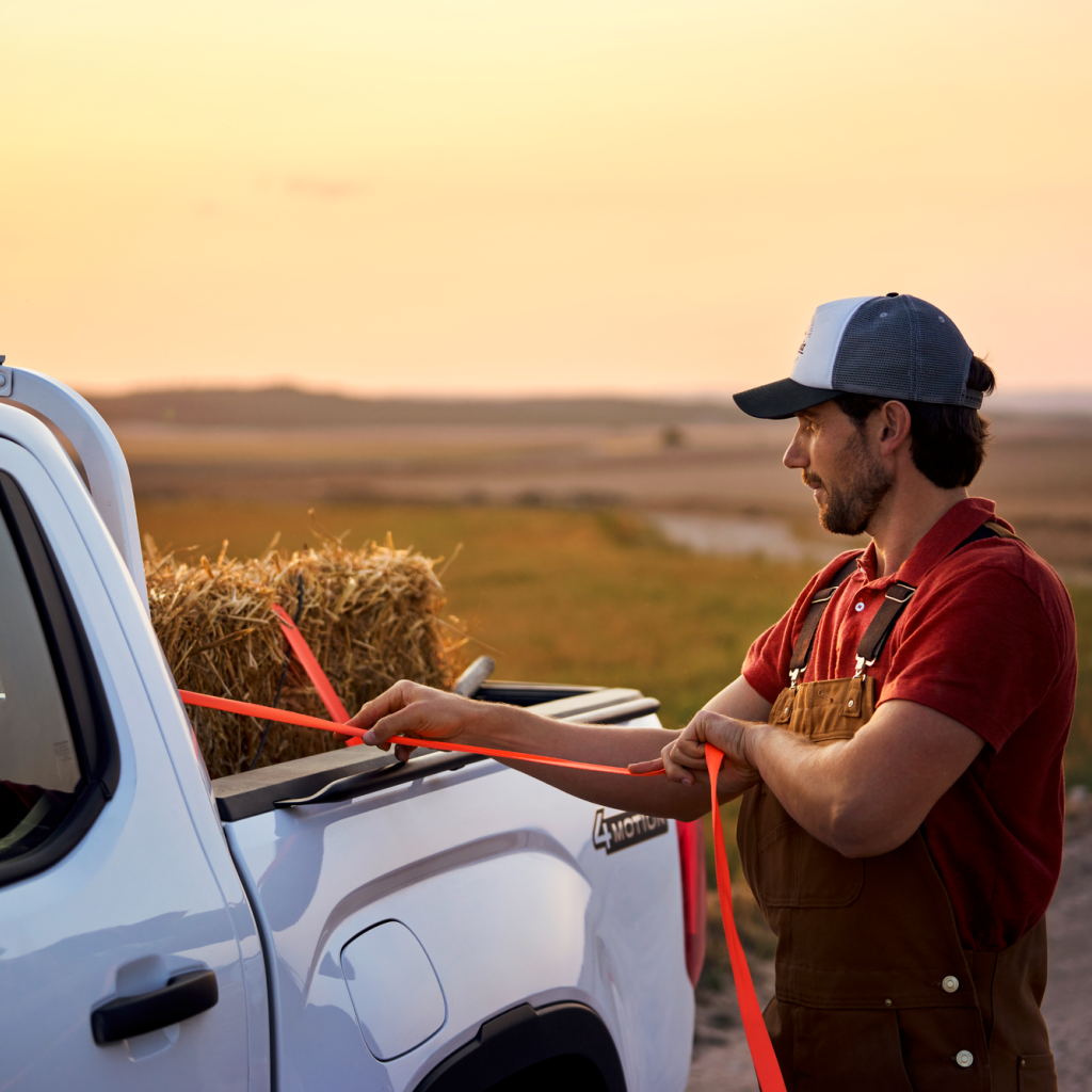 Muž přivazuje balík slámy na ložnou plochu Volkswagenu Amarok.
